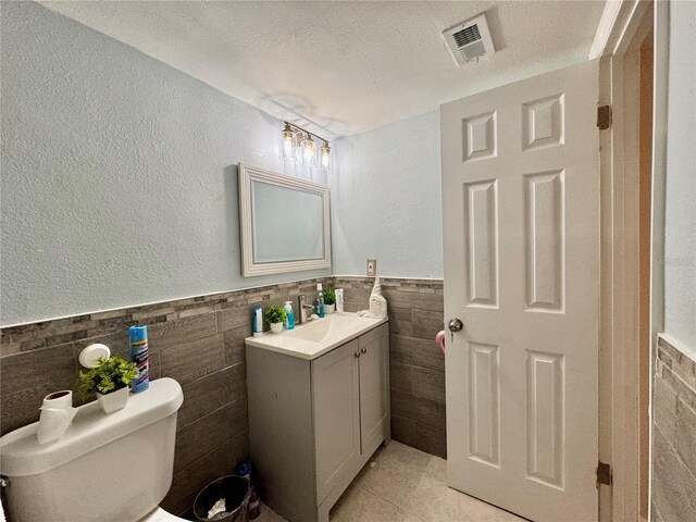 bathroom featuring toilet, tile patterned flooring, vanity, a textured ceiling, and tile walls