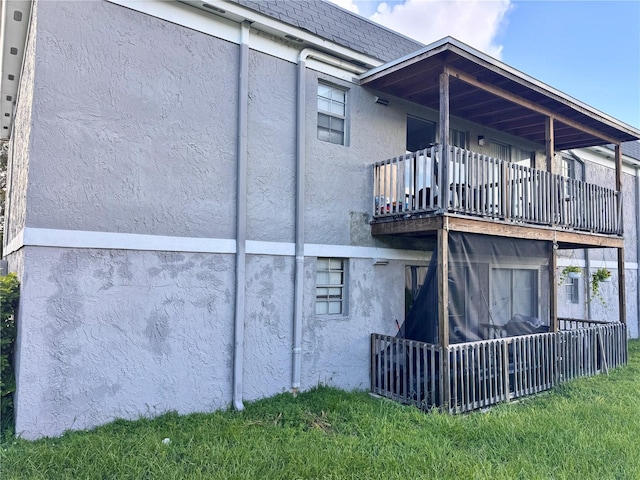 rear view of property featuring a lawn, a balcony, and stucco siding