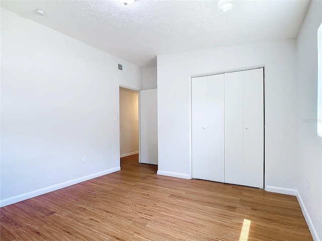 unfurnished bedroom featuring light wood-type flooring, a closet, and a textured ceiling