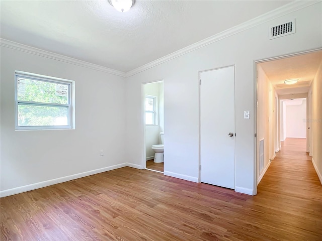 unfurnished bedroom featuring ensuite bath, ornamental molding, wood-type flooring, and multiple windows