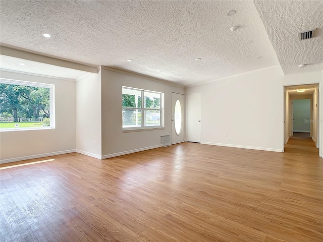 unfurnished living room featuring hardwood / wood-style flooring, a textured ceiling, plenty of natural light, and ornamental molding