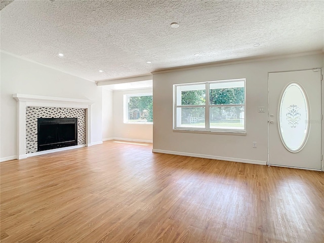 unfurnished living room with light wood-type flooring, a tile fireplace, and a textured ceiling