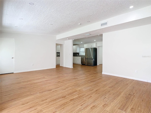 unfurnished living room with light wood-type flooring and a textured ceiling