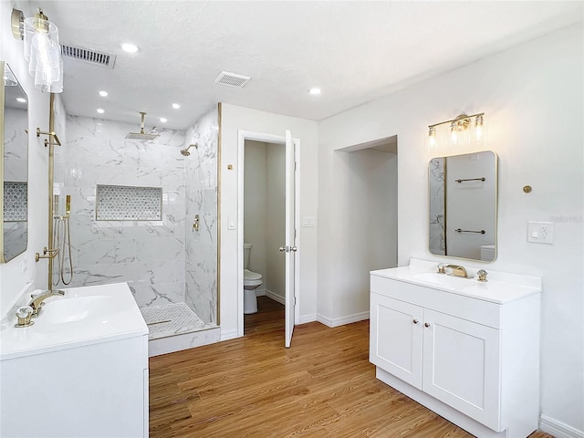 bathroom featuring toilet, vanity, a tile shower, and wood-type flooring