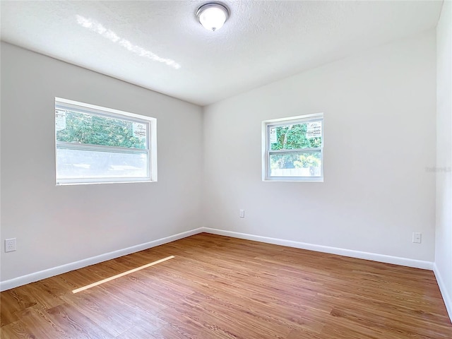 empty room with a textured ceiling, lofted ceiling, plenty of natural light, and wood-type flooring