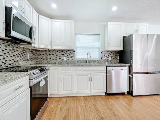 kitchen with appliances with stainless steel finishes, sink, light stone counters, light wood-type flooring, and white cabinetry