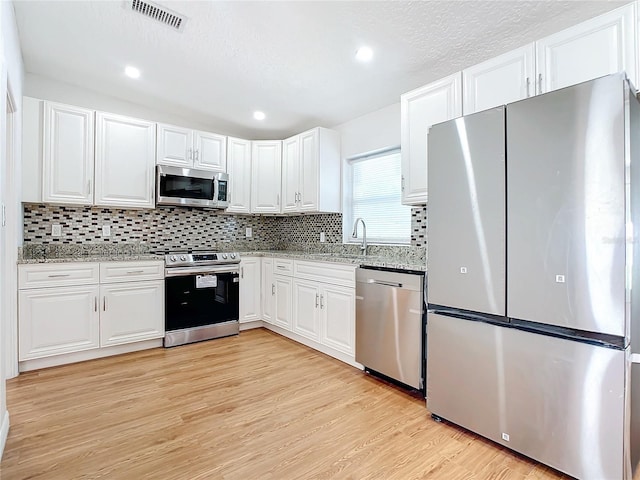 kitchen featuring appliances with stainless steel finishes, sink, light stone counters, light wood-type flooring, and white cabinets