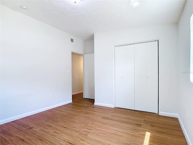 unfurnished bedroom featuring light wood-type flooring, a textured ceiling, and a closet