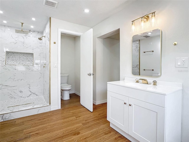 bathroom with toilet, a tile shower, hardwood / wood-style floors, and vanity