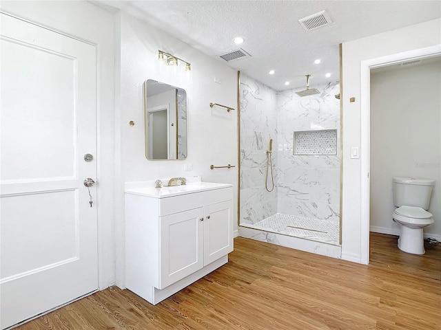 bathroom featuring toilet, wood-type flooring, tiled shower, a textured ceiling, and vanity