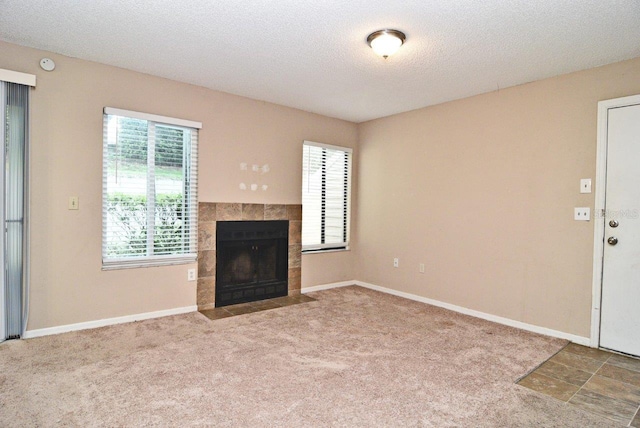 unfurnished living room featuring carpet flooring, a textured ceiling, and a tile fireplace