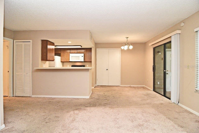 kitchen featuring white appliances, a notable chandelier, light carpet, kitchen peninsula, and a textured ceiling