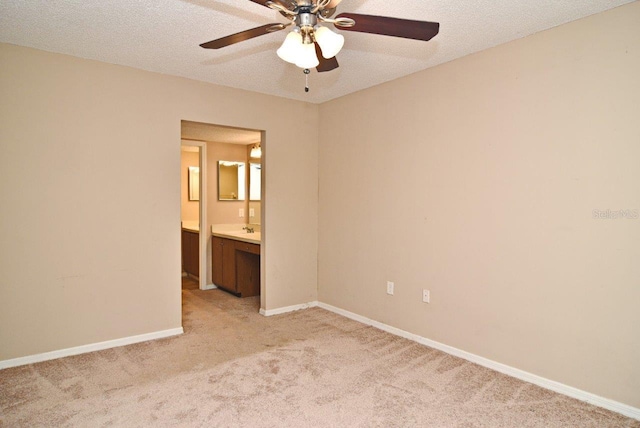 unfurnished bedroom featuring a textured ceiling, connected bathroom, sink, ceiling fan, and light colored carpet