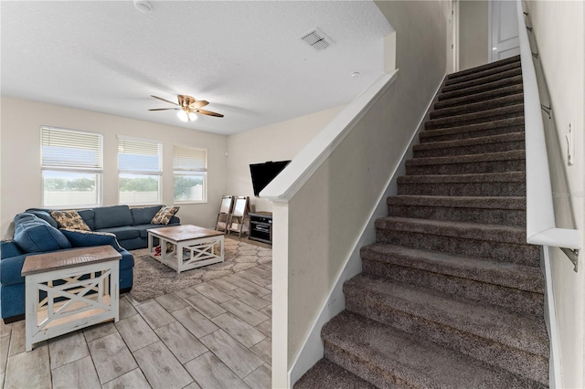 stairway with ceiling fan, wood-type flooring, and a textured ceiling