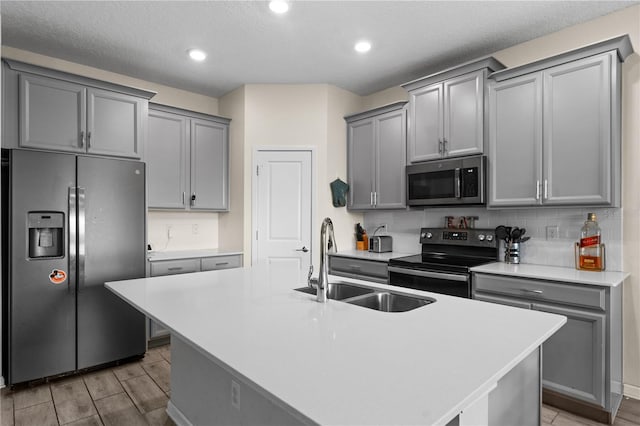 kitchen featuring tasteful backsplash, a kitchen island with sink, stainless steel appliances, sink, and hardwood / wood-style flooring