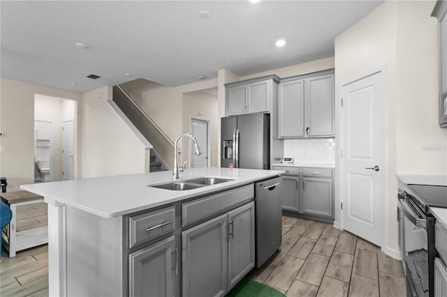 kitchen with gray cabinetry, light hardwood / wood-style flooring, stainless steel appliances, sink, and a kitchen island with sink