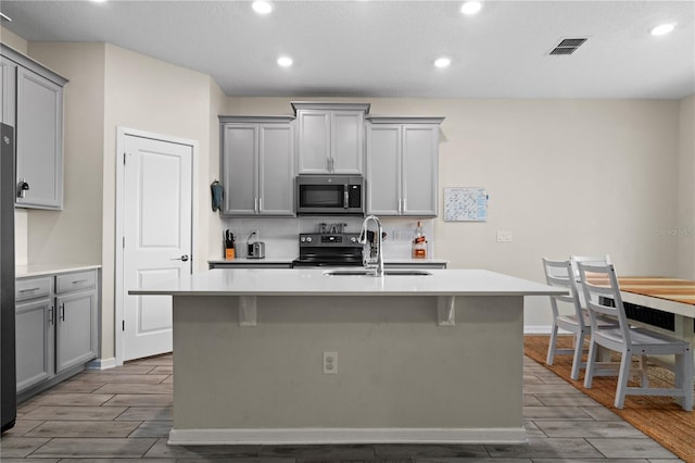 kitchen featuring light wood-type flooring, stainless steel appliances, sink, gray cabinets, and a kitchen island with sink