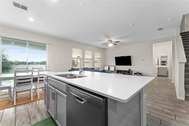 kitchen featuring light hardwood / wood-style flooring, a center island with sink, sink, ceiling fan, and stainless steel dishwasher