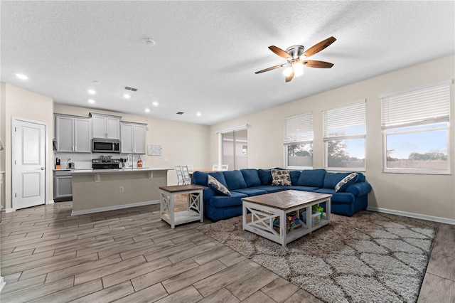 living room featuring a textured ceiling, light hardwood / wood-style flooring, and ceiling fan