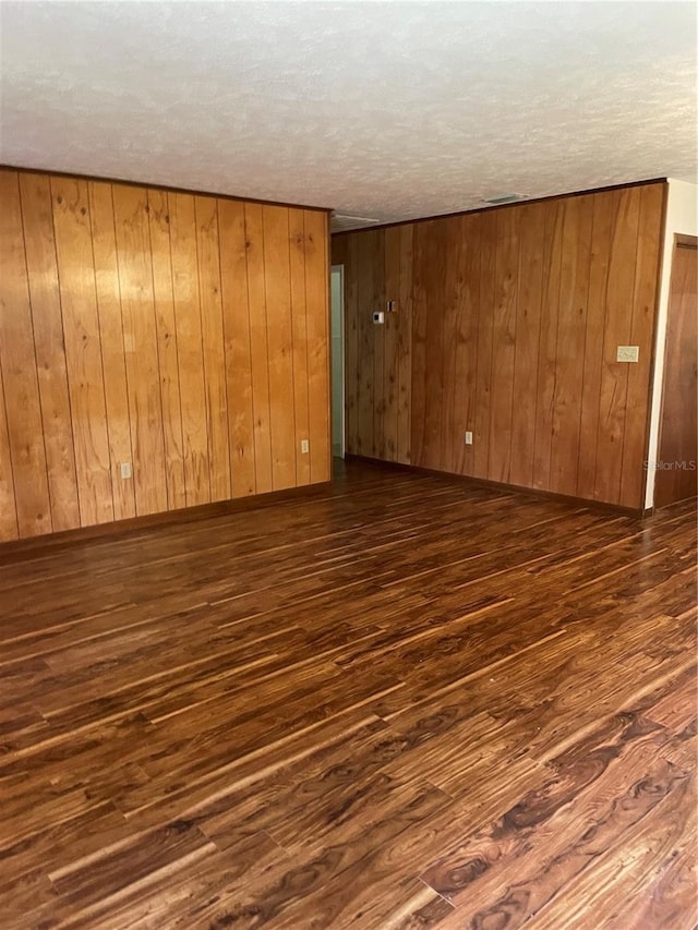 spare room featuring dark wood-type flooring, a textured ceiling, and wood walls