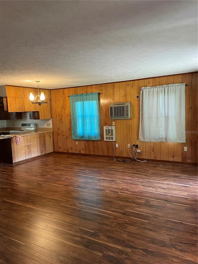 unfurnished living room featuring a wall unit AC, wooden walls, a notable chandelier, dark hardwood / wood-style floors, and a textured ceiling