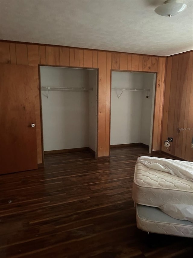 unfurnished bedroom with multiple closets, dark wood-type flooring, a textured ceiling, and wooden walls