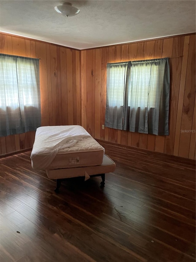 bedroom with a textured ceiling, dark wood-type flooring, and wooden walls