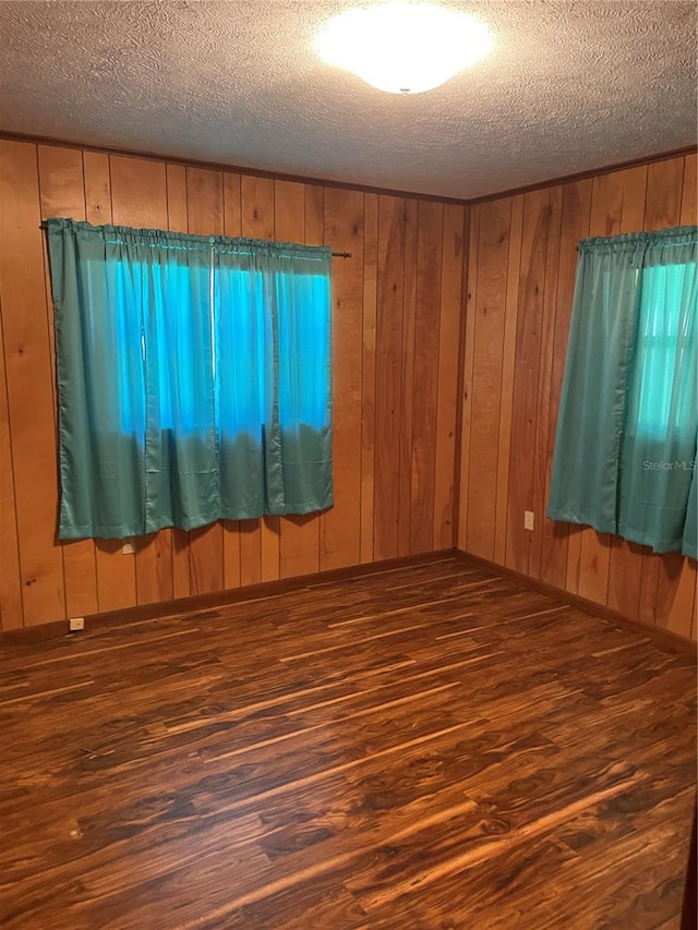 unfurnished room featuring dark wood-type flooring, a textured ceiling, and wooden walls