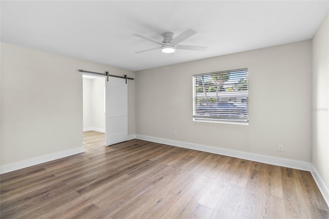 unfurnished room featuring a barn door, hardwood / wood-style floors, and ceiling fan