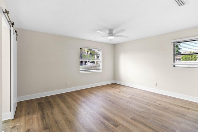 interior space featuring a barn door, multiple windows, ceiling fan, and wood-type flooring