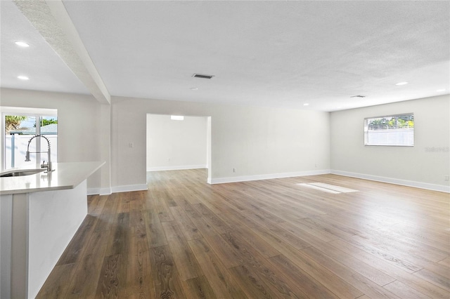 unfurnished living room featuring a textured ceiling, wood-type flooring, sink, and beam ceiling