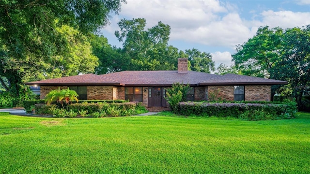 view of front of house with brick siding, a chimney, and a front yard