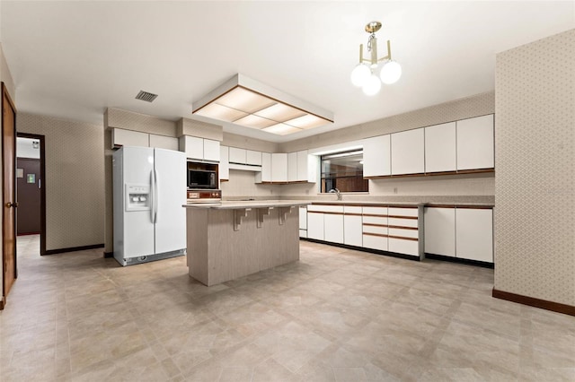 kitchen featuring white refrigerator with ice dispenser, a kitchen bar, a center island, white cabinetry, and black microwave