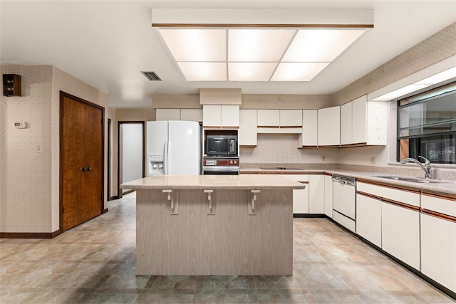 kitchen with white cabinets, sink, black appliances, a kitchen island, and a breakfast bar