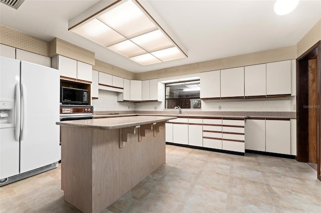 kitchen with white cabinetry, a kitchen island, black microwave, and white fridge with ice dispenser