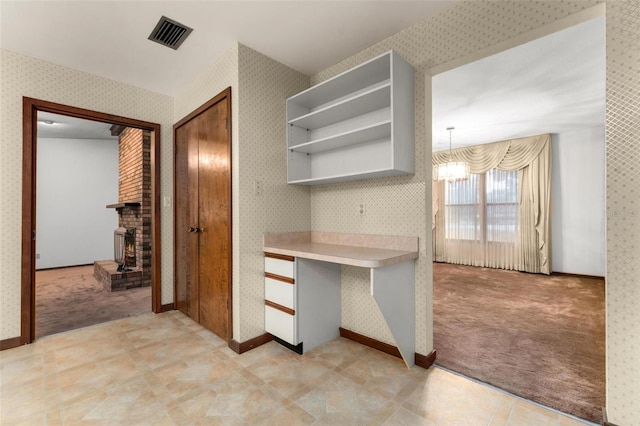 kitchen with light colored carpet, a notable chandelier, and a fireplace