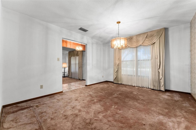 spare room featuring a chandelier, carpet, and a textured ceiling