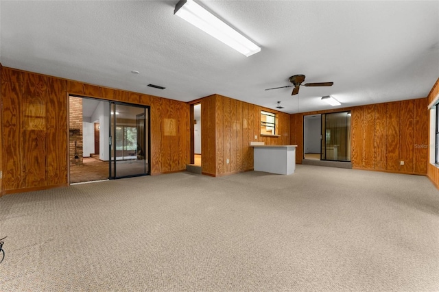 unfurnished living room with carpet flooring, wood walls, ceiling fan, and a textured ceiling