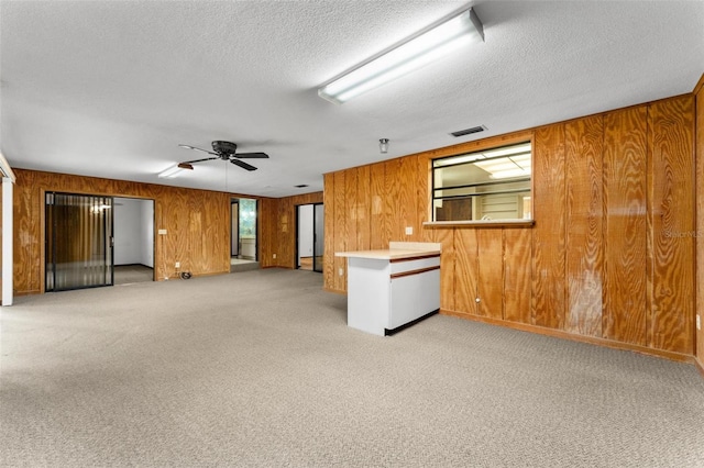 interior space with a textured ceiling, carpet flooring, ceiling fan, and wood walls