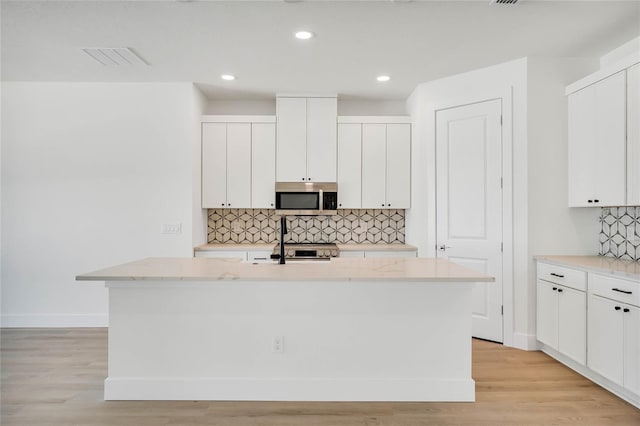 kitchen with white cabinets, a center island with sink, light hardwood / wood-style flooring, and backsplash