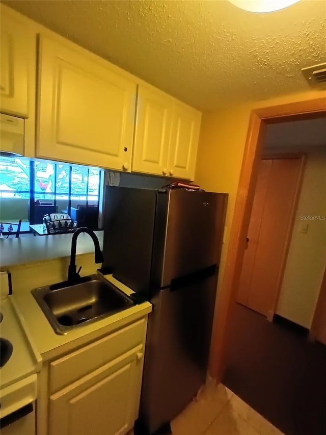 kitchen featuring visible vents, white cabinetry, freestanding refrigerator, a textured ceiling, and a sink