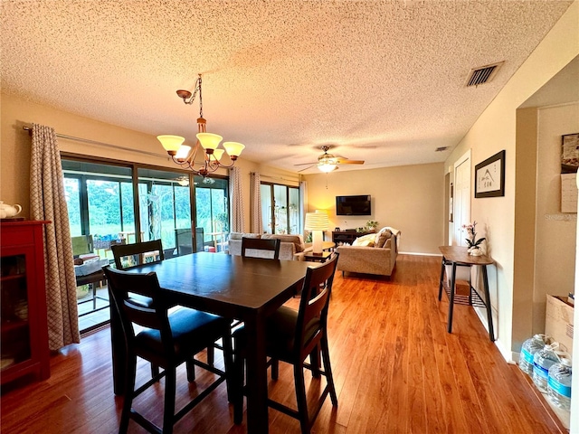 dining space featuring ceiling fan with notable chandelier, wood-type flooring, and a textured ceiling