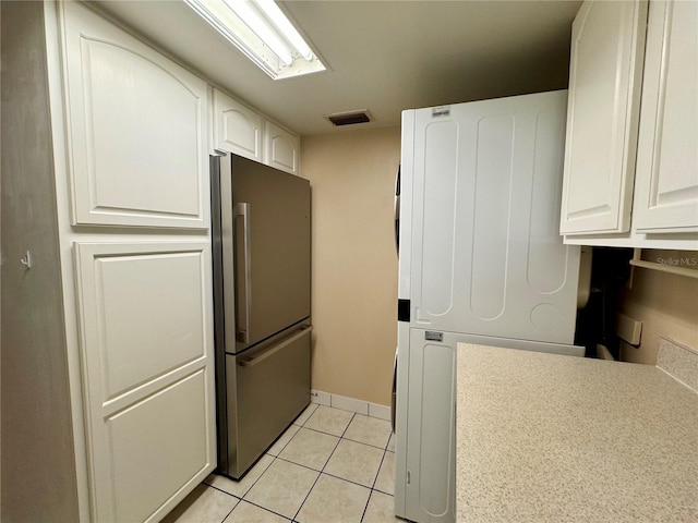 kitchen featuring washer / dryer, stainless steel refrigerator, light tile patterned floors, and white cabinetry