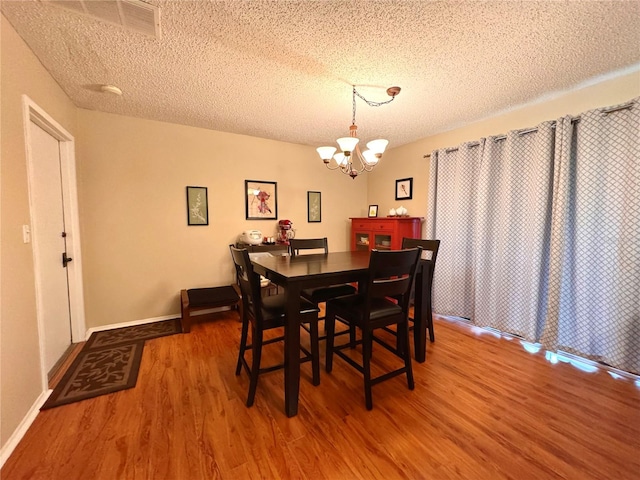 dining area featuring a textured ceiling, hardwood / wood-style floors, and a notable chandelier