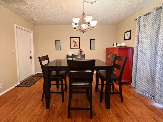 dining space with a textured ceiling, an inviting chandelier, and hardwood / wood-style flooring