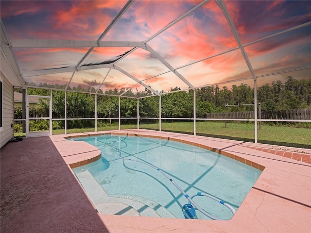 pool at dusk with glass enclosure, a lawn, and a patio