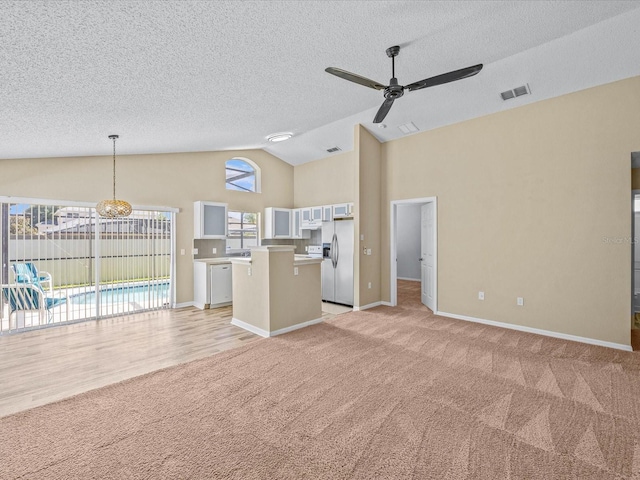 2977 Kokomo Loop, Haines City, FL 33844 - unfurnished living room with light colored carpet, a ceiling fan, a textured ceiling, high vaulted ceiling, and a chandelier
