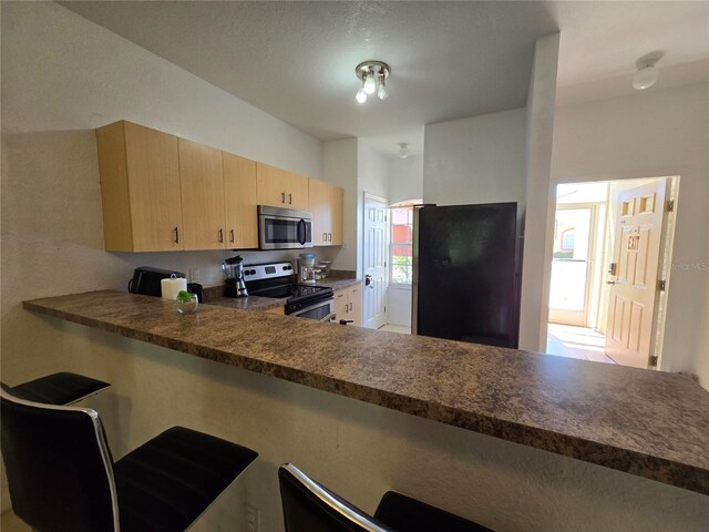 kitchen with appliances with stainless steel finishes, light brown cabinets, kitchen peninsula, and a textured ceiling