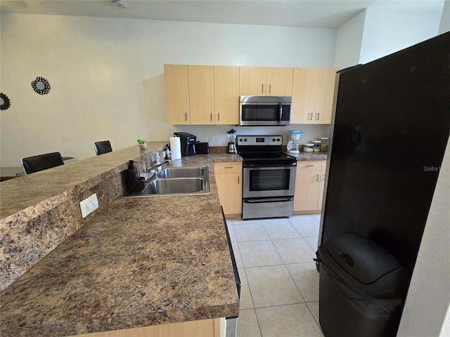 kitchen featuring light tile patterned floors, light brown cabinets, stainless steel appliances, a peninsula, and a sink