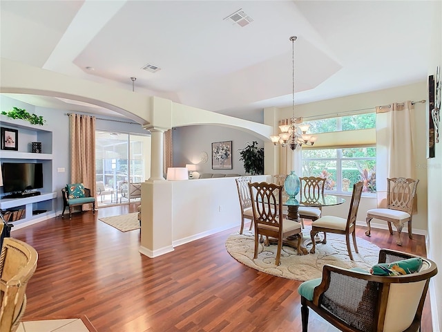 dining room featuring decorative columns, dark hardwood / wood-style floors, an inviting chandelier, and a raised ceiling